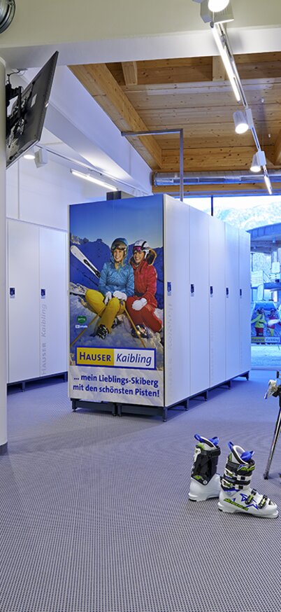 Skidepot am Hauser Kaibling mit weißen Schließfächern, abgestellten Skischuhen und einem Poster mit Wintersportlern. | © Andy Sillaber