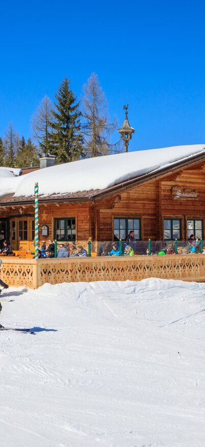 Skiers in front of the Schmiedhütte at Hauser Kaibling on a sunny winter's day with a clear mountain backdrop. | © Hauser Kaibling