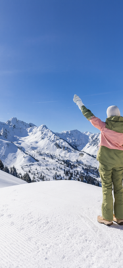 Zwei Personen in bunter Winterkleidung stehen auf einem verschneiten Berggipfel mit erhobenen Armen und blicken auf die umliegenden Alpen. Strahlend blauer Himmel und verschneite Berge erstrecken sich bis zum Horizont. | © Originalfoto Bernhard Moser | bearbeitet mit KI/Photoshop